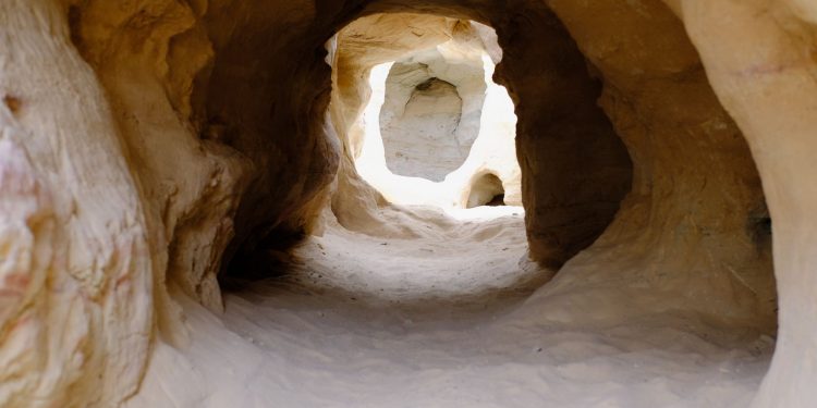 Explore a naturally eroded sandstone tunnel with sunlight filtering through, showcasing intricate geological formations.
