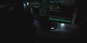 Dark room setup with code displayed on PC monitors highlighting cybersecurity themes.