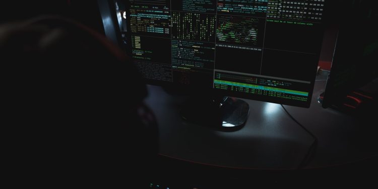 Dark room setup with code displayed on PC monitors highlighting cybersecurity themes.