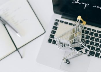 Creative depiction of online shopping with a miniature cart on a laptop keyboard.
