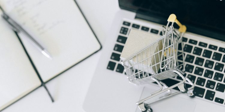 Creative depiction of online shopping with a miniature cart on a laptop keyboard.