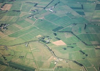 Expansive aerial view of green agricultural fields with scattered farmhouses and winding pathways.