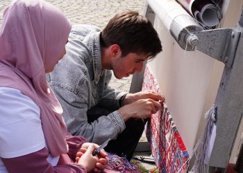 Detailed view of artisans weaving a traditional carpet outdoors, showcasing craftsmanship and cultural heritage.