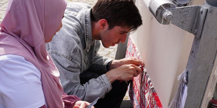 Detailed view of artisans weaving a traditional carpet outdoors, showcasing craftsmanship and cultural heritage.