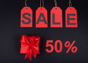 Red gift box next to sale tags and 50% sign on black background, ideal for promotions.