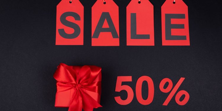 Red gift box next to sale tags and 50% sign on black background, ideal for promotions.