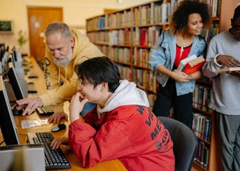 Students collaborating and learning in a library setting, engaging with computers and books.