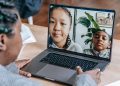 Back view of crop anonymous attentive African American teacher answer questions of pupils online on laptop