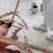 An artist uses a brush to paint abstract patterns on a large canvas placed on the floor.
