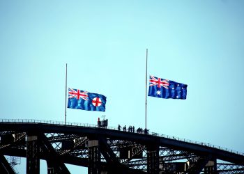 Australian and New South Wales flags flying on Sydney Harbour Bridge silhouette.