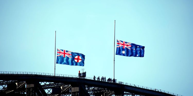 Australian and New South Wales flags flying on Sydney Harbour Bridge silhouette.