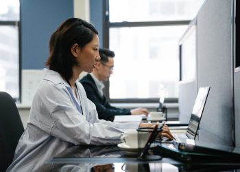 Two professionals working diligently on laptops in a modern office setup, capturing productivity and teamwork.