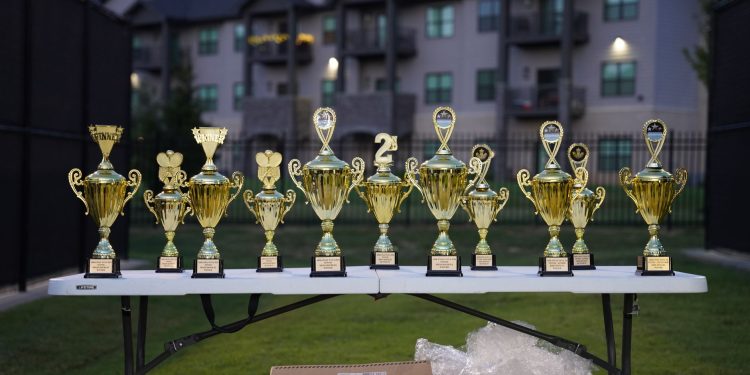 Lineup of gold trophies on a table outdoors with apartment backdrop.
