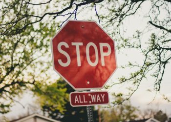 A clear red stop sign with 'All Way' below it in a sunny suburban setting.