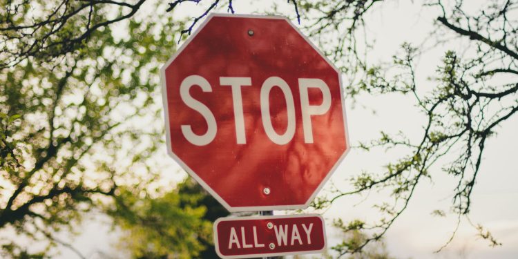 A clear red stop sign with 'All Way' below it in a sunny suburban setting.
