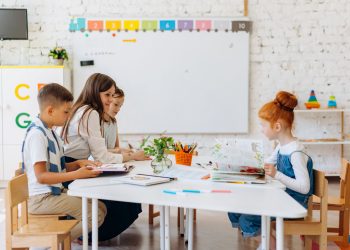 Students and teacher interacting in a bright, colorful classroom setting.