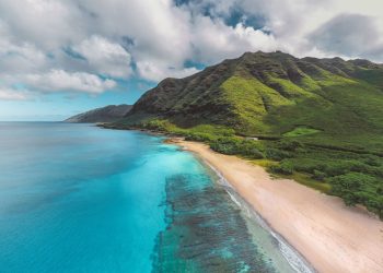 Stunning aerial view of a vibrant Hawaiian coastline with lush mountains and crystal-clear waters.