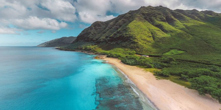 Stunning aerial view of a vibrant Hawaiian coastline with lush mountains and crystal-clear waters.