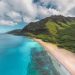 Stunning aerial view of a vibrant Hawaiian coastline with lush mountains and crystal-clear waters.