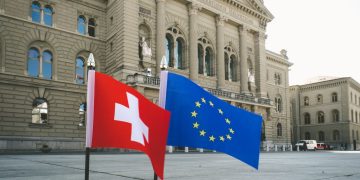 Front view of Swiss Parliament Building in Bern with Swiss and EU flags.