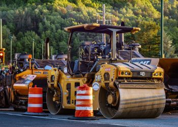 Construction machinery and vehicles on site with road rollers and cones.