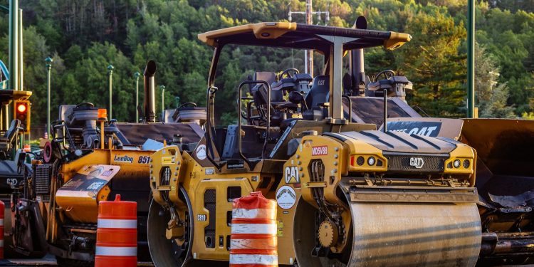 Construction machinery and vehicles on site with road rollers and cones.