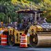 Construction machinery and vehicles on site with road rollers and cones.