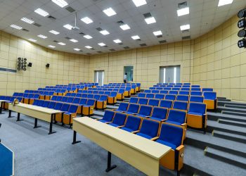 Spacious lecture hall with blue seats and desks ready for students.