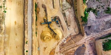An aerial shot of an open-pit mine with machinery and pathways visible, surrounded by landscape.