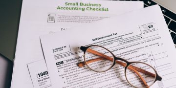 Close-up of tax forms and a small business accounting checklist on a laptop.