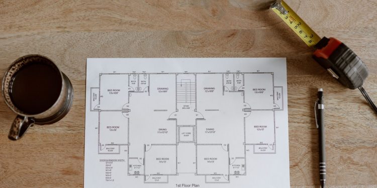 Top view of set of plan of room with tape measure and pen for work for architect with cup with coffee on wooden table in soft daylight
