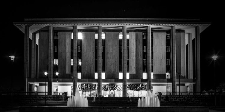 Monochrome image showcasing the National Library of Australia with illuminating fountains at night.