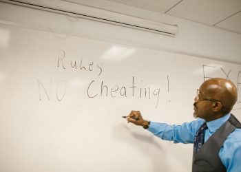 Teacher writes 'No Cheating!' on whiteboard during classroom instruction.