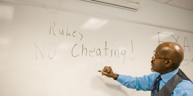 Teacher writes 'No Cheating!' on whiteboard during classroom instruction.