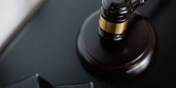 From above of wooden gavel on round surface near folders on table in courtroom