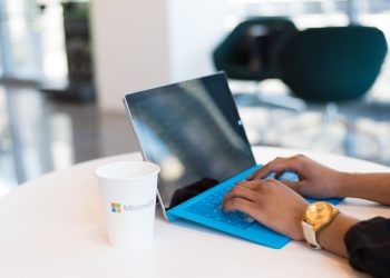 Hands typing on a blue keyboard with a branded cup on a table.