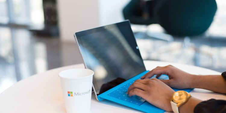Hands typing on a blue keyboard with a branded cup on a table.