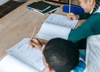 From above of diverse smart boy and girl doing tasks and writing on papers at classroom desk