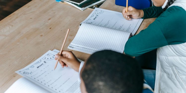 From above of diverse smart boy and girl doing tasks and writing on papers at classroom desk