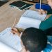 From above of diverse smart boy and girl doing tasks and writing on papers at classroom desk
