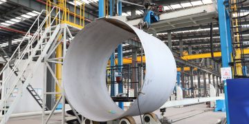 A spacious industrial factory scene showcasing steel pipe production with modern machinery.