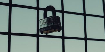 Close-up of a steel padlock on a mesh fence, symbolizing protection and security.