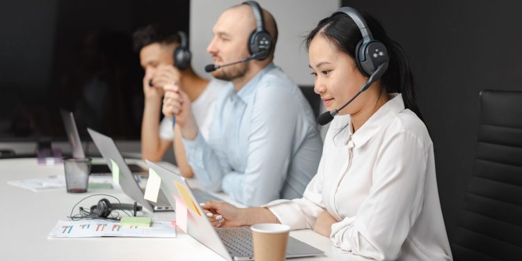 Call center agents wearing headsets working on laptops at a customer support team meeting.