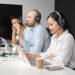Call center agents wearing headsets working on laptops at a customer support team meeting.