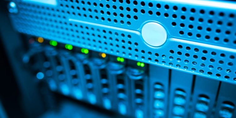 Focused view of a modern data server rack with blinking lights in a blue-lit environment.
