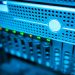 Focused view of a modern data server rack with blinking lights in a blue-lit environment.