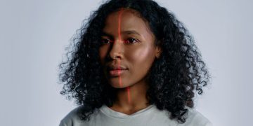 Portrait of a woman with facial recognition technology lines across her face on a plain background.