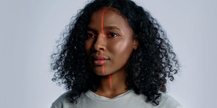 Portrait of a woman with facial recognition technology lines across her face on a plain background.