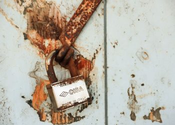 Close-up of a rusty padlock on a weathered wall, showcasing vintage charm.
