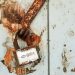 Close-up of a rusty padlock on a weathered wall, showcasing vintage charm.